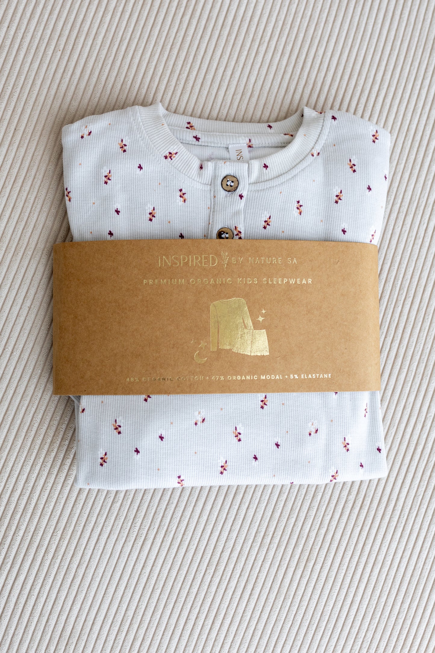 Inspired by Nature SA organic kids' sleepwear in light grey with a tiny floral print, folded neatly with branded kraft paper packaging. Made with premium sustainable fabrics for soft and safe sleep.