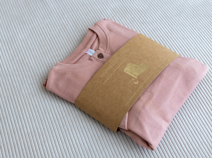 Inspired by Nature SA organic cotton pyjamas in a soft rose pink hue, folded with branded kraft packaging. Gentle on skin and made for kids' comfort using sustainable materials.


